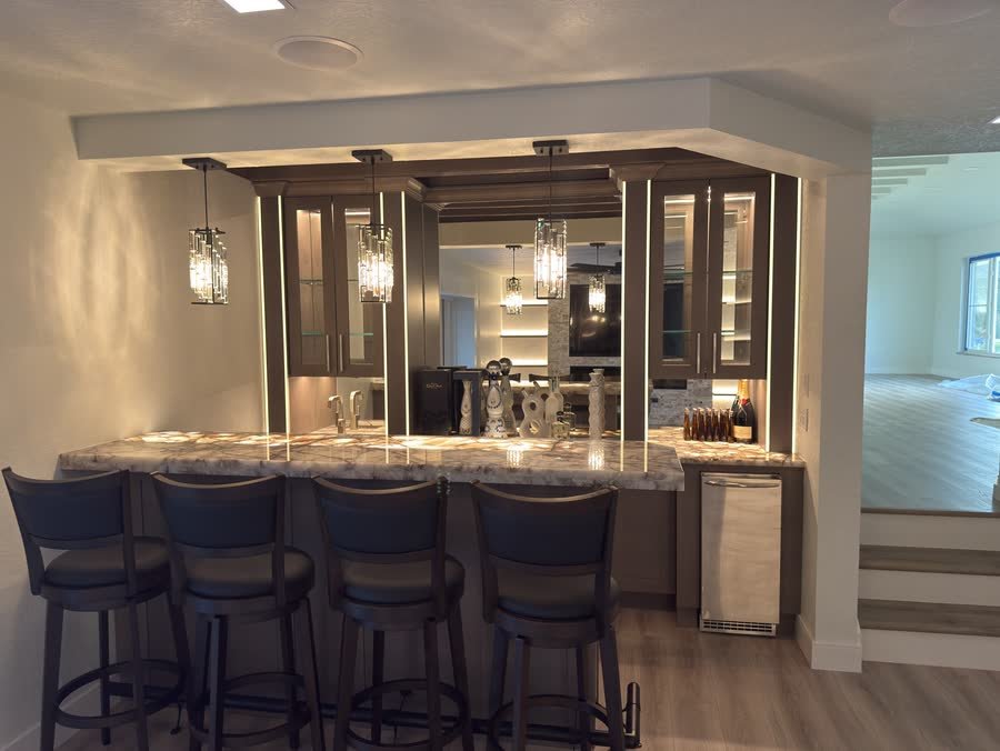 Custom home bar with a backlit stone counter and crystal pendants