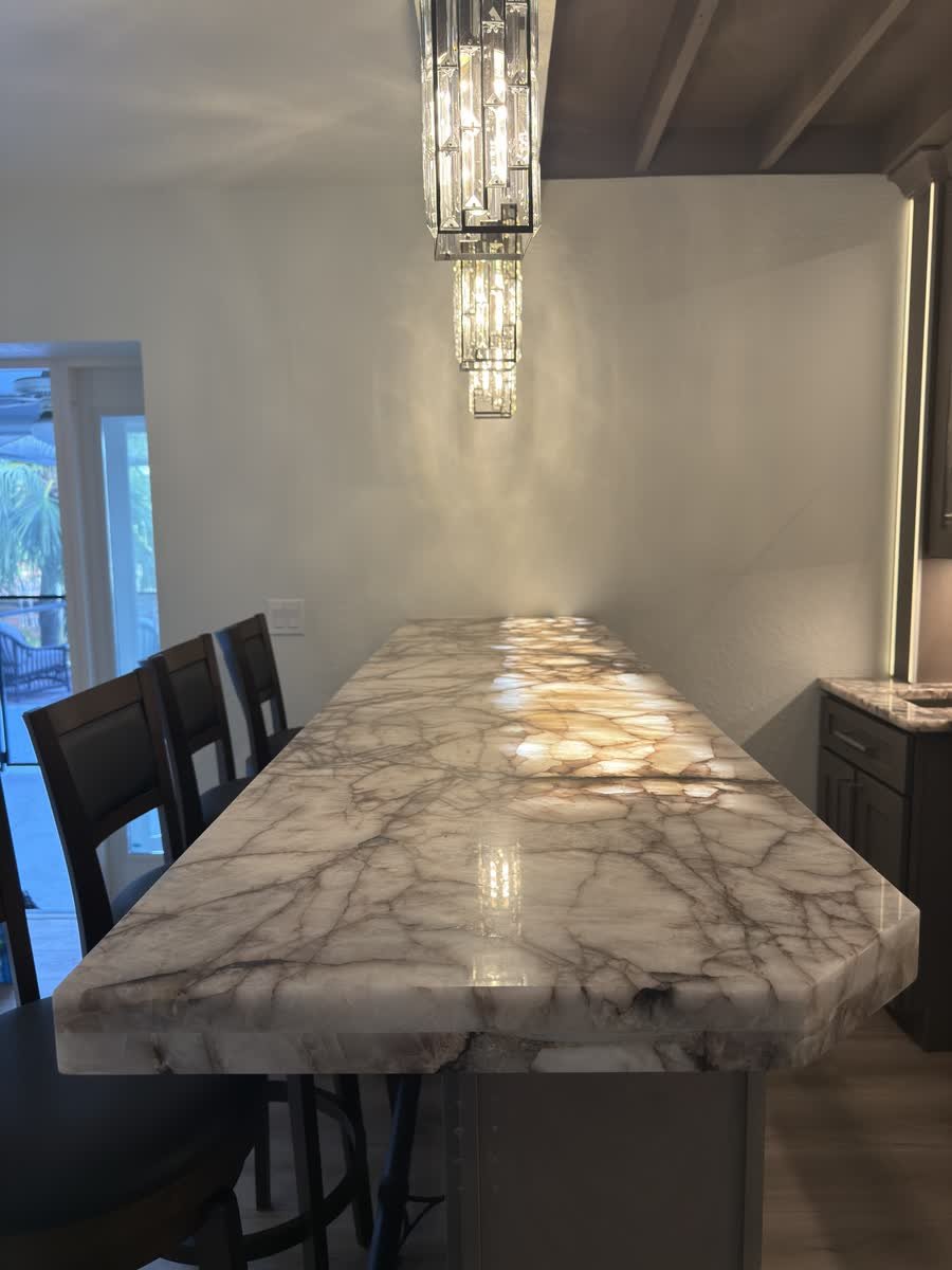 Backlit stone bar peninsula with seating under a crystal pendant