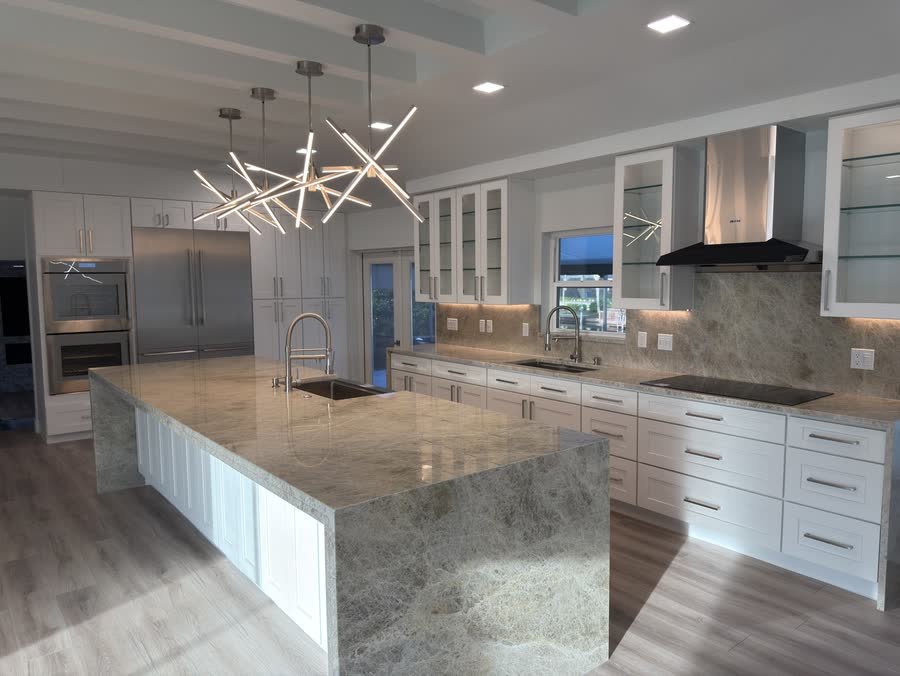 Finished kitchen with a stone waterfall island, white cabinets and starburst lights