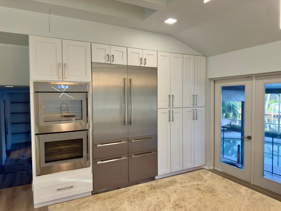 Kitchen wall with double wall ovens, a built-in refrigerator and white pantry cabinets