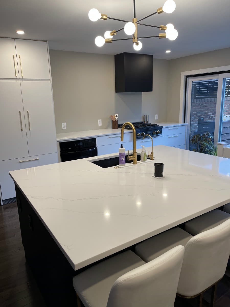Kitchen island with a white quartz top, brass faucet and a modern brass chandelier