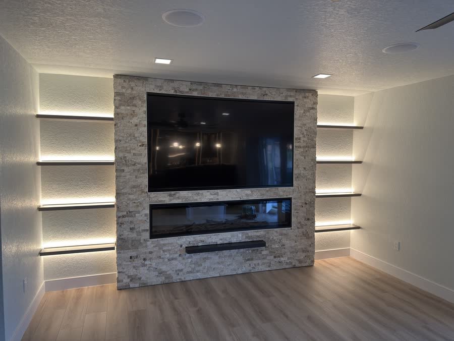 Stacked stone media wall with a TV, linear fireplace and lit floating shelves