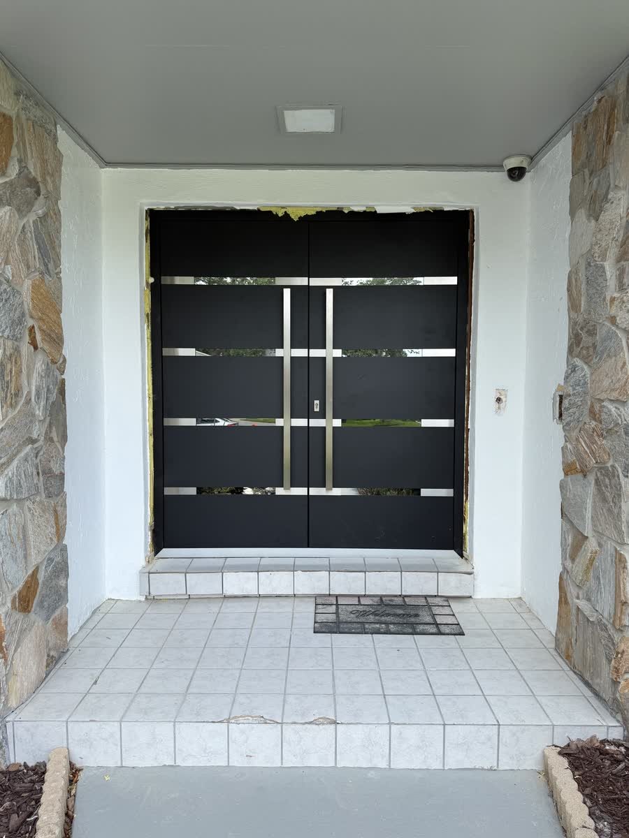 New modern black double entry door with stainless bar handles in a stone-clad entry