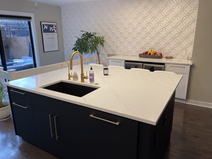 Navy blue kitchen island with a white quartz top, brass pulls and a gold faucet