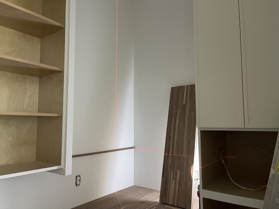 Pantry build with white cabinets set to a red laser level line and a butcher block top waiting to go in