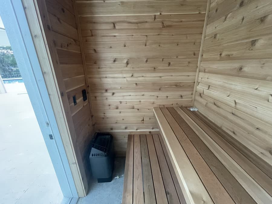 Finished cedar sauna with the heater beside the benches and the glass door to the pool