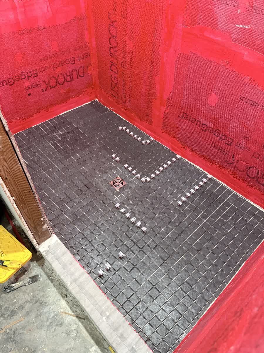Shower walls coated in red waterproofing membrane with a black mosaic floor going in