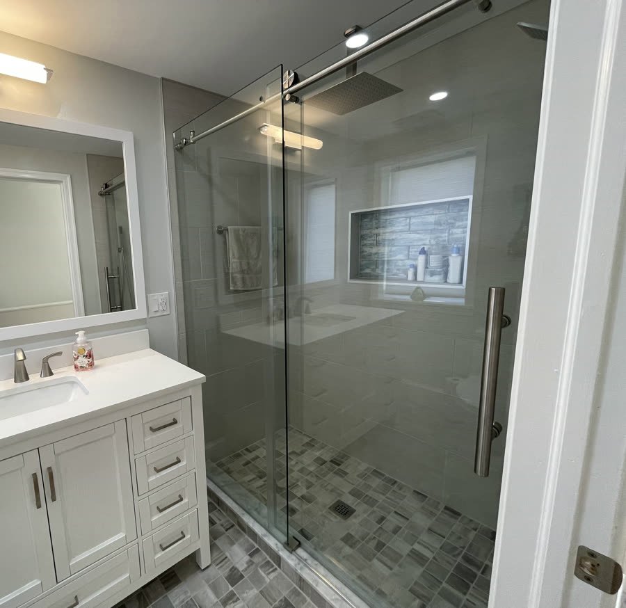Walk-in shower with a tiled niche and a glass door beside a white vanity