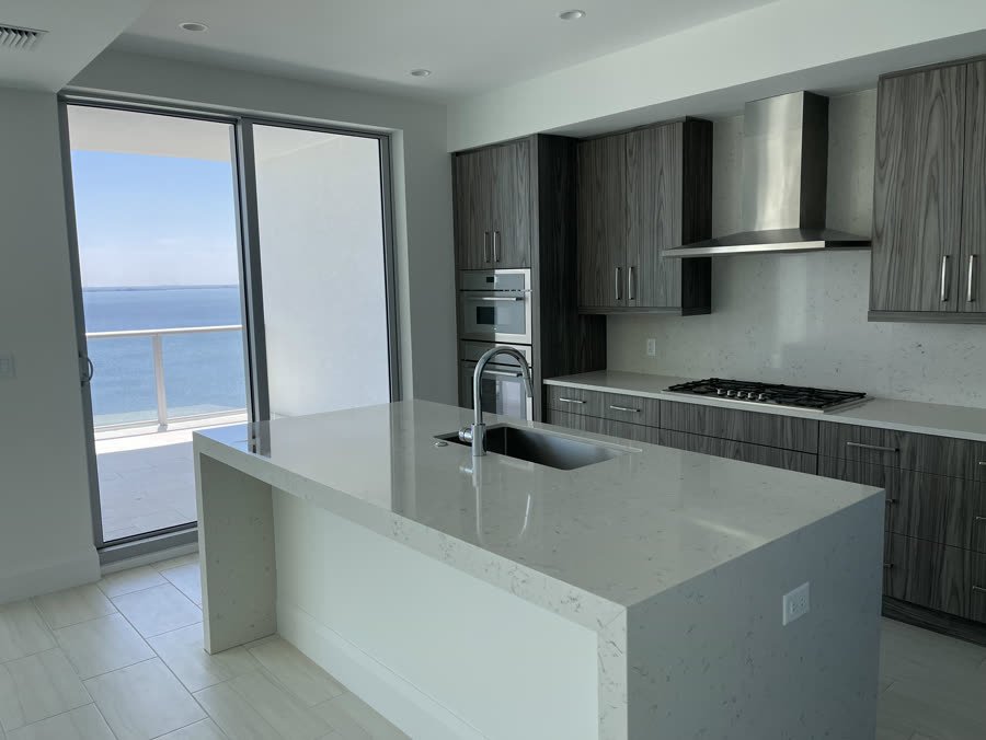 Condo kitchen remodel with grey wood cabinets and a white waterfall island facing the water