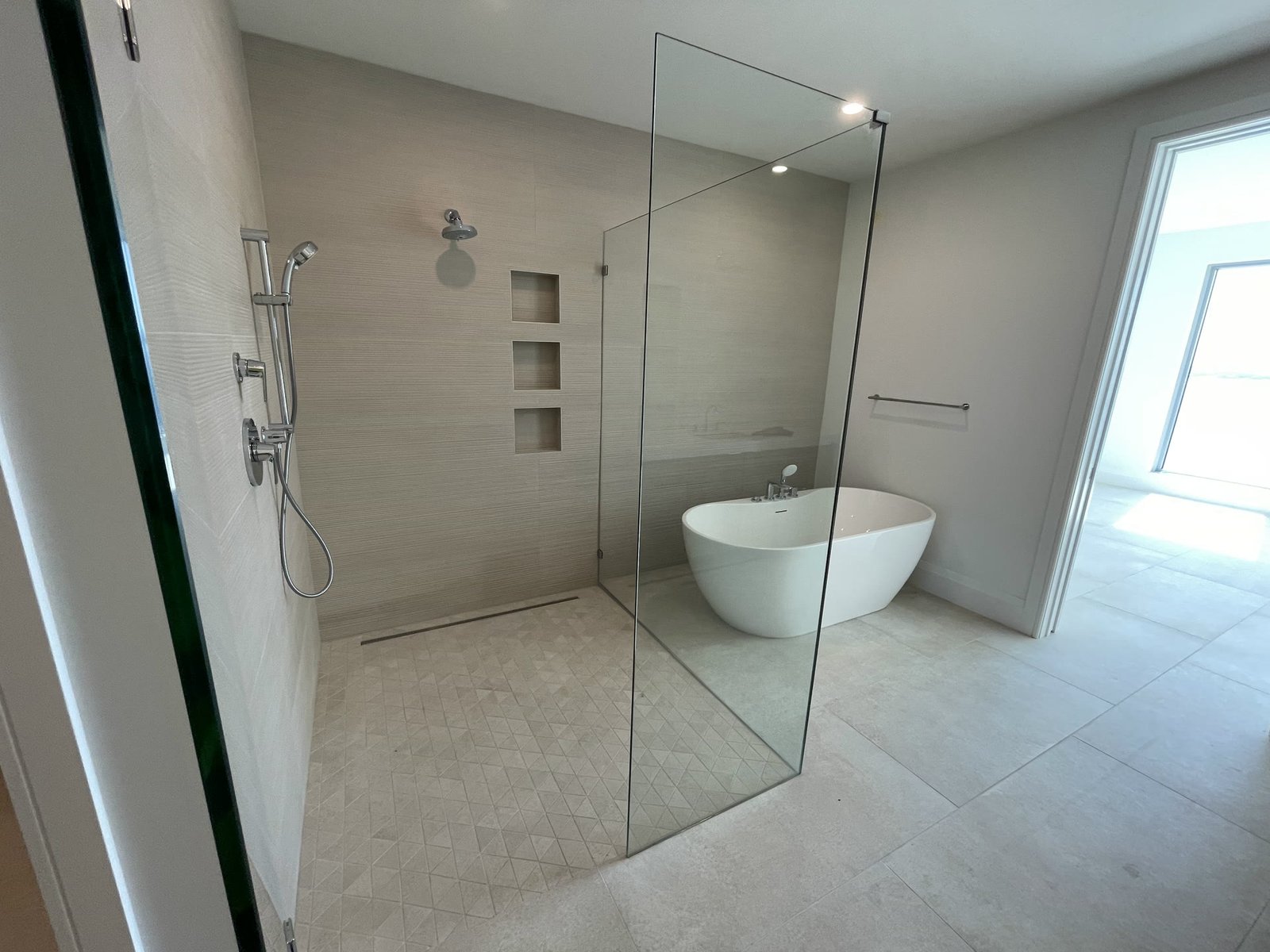 Remodeled Tampa bathroom with a curbless shower, glass panel and freestanding tub